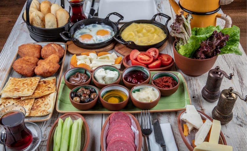 Mesa de desayuno turco con huevos, quesos, aceitunas, mermeladas, pan recién hecho y té servido en vaso de tulipa