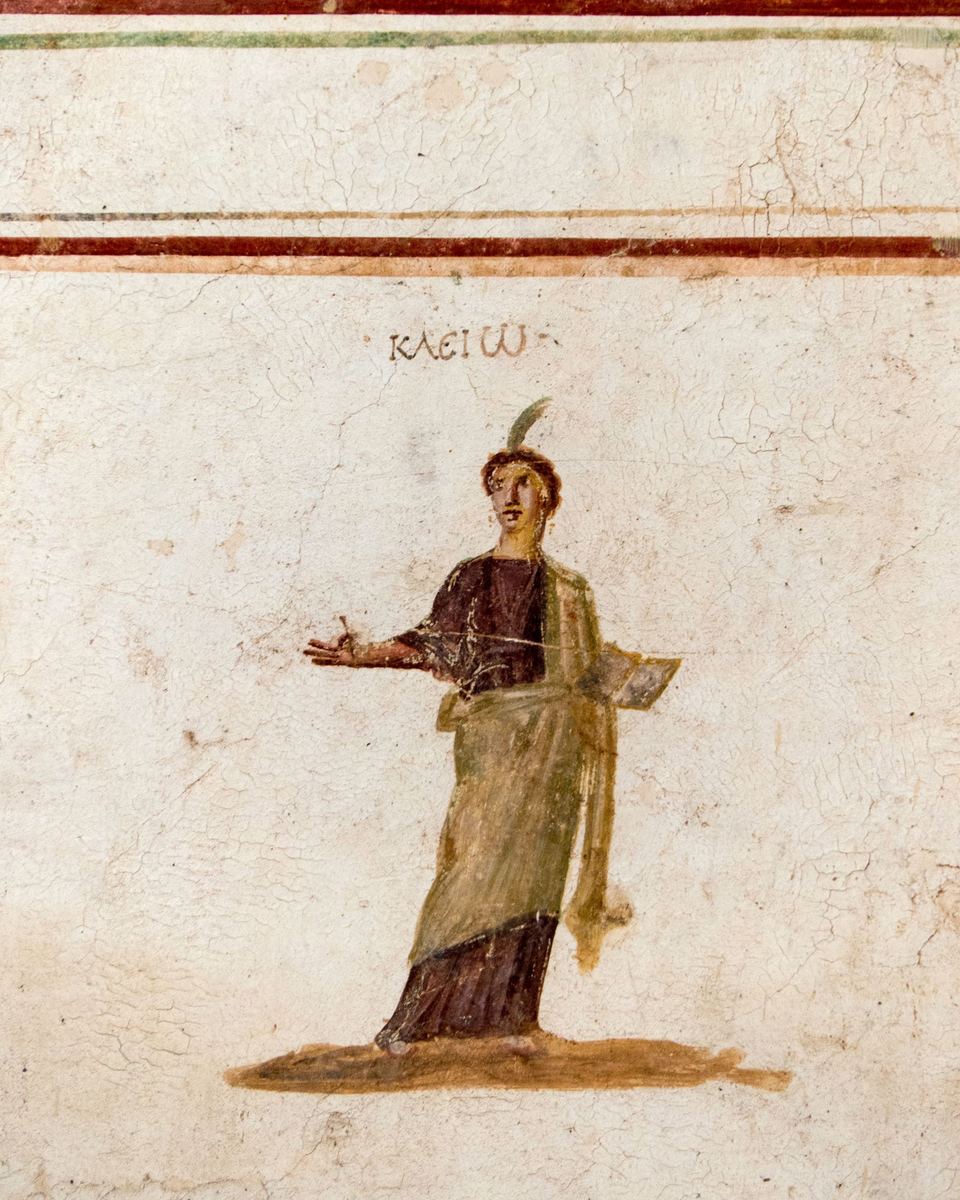 Fresco romano de la musa Clío, de pie con un libro abierto y su nombre pintado en griego encima, en una pared de las Casas de la Ladera de Éfeso